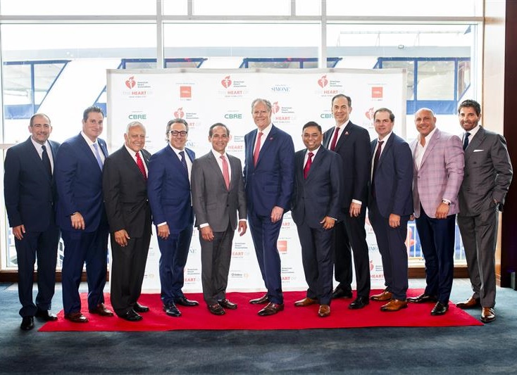 Eleven men standing in front of the American Heart Association The Heart of New York City step and repeat banner.